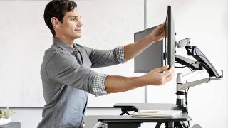 Mejores brazos de monitor: hombre ajustando el monitor en el brazo del monitor