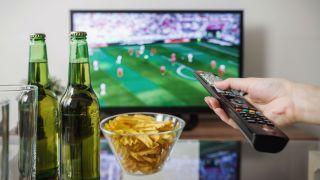A távirányítóval kézzel nézheti a Super Bowlt a tévében sörösüvegekkel és harapnivalókkal