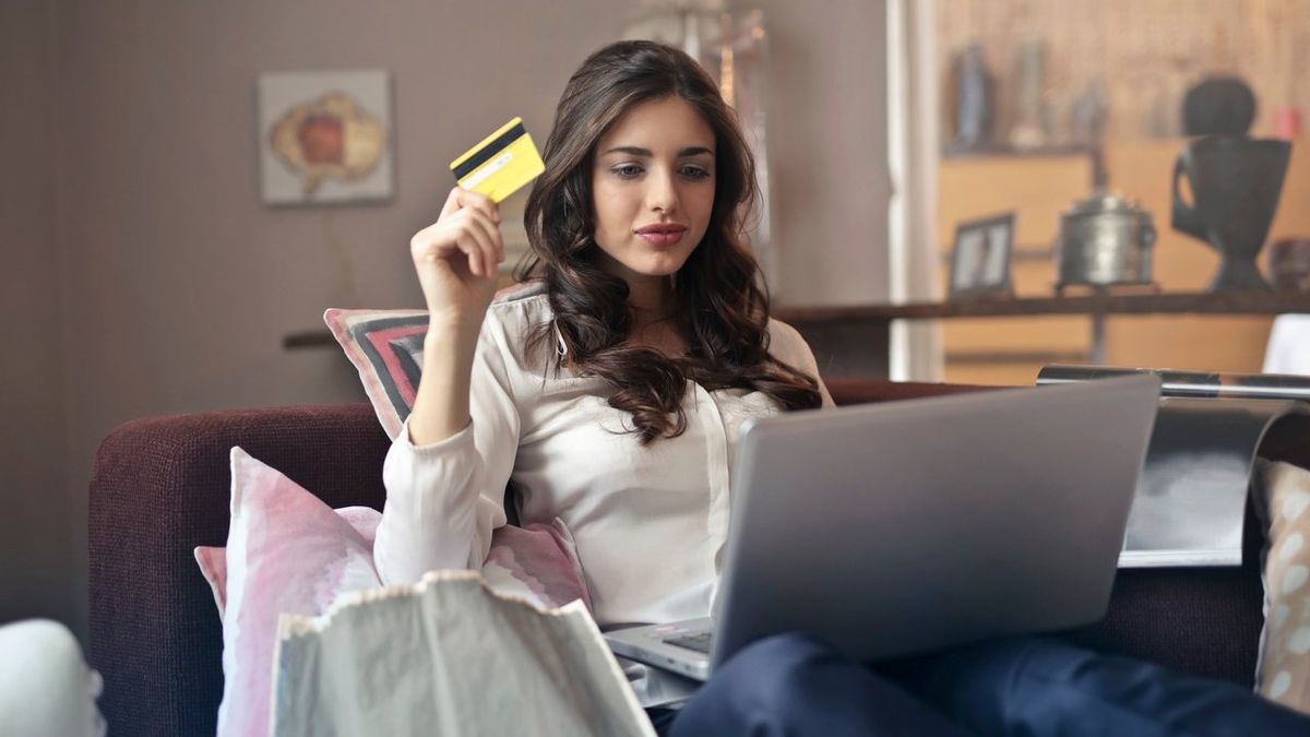 Frau am Laptop winkt Kreditkarte